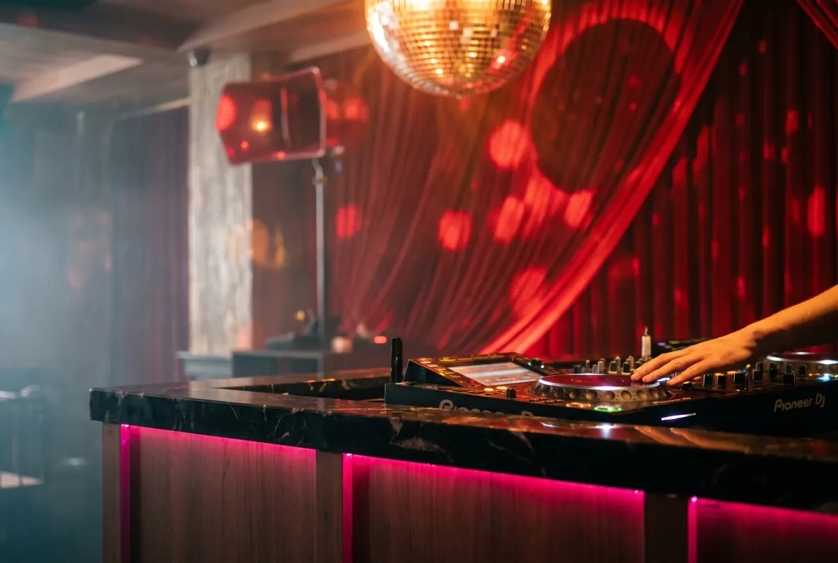 The DJ booth at Baccarat Bangkok — Pioneer CDJs on a black marble counter with pink light underneath and red curtains behind