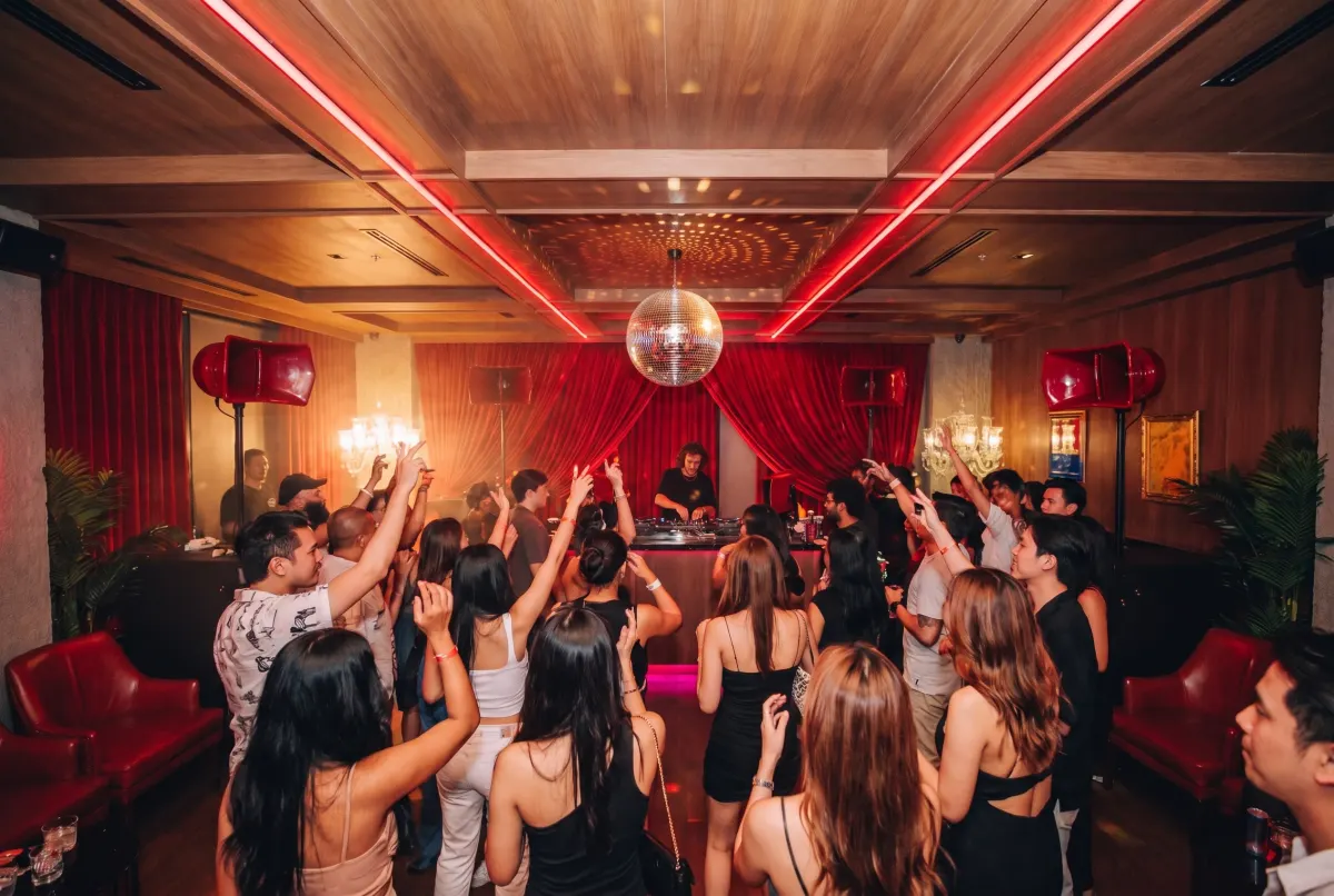 Inside Baccarat Bangkok — red neon strips on a wood ceiling, disco ball, red velvet curtains and red horn speakers over a busy dance floor