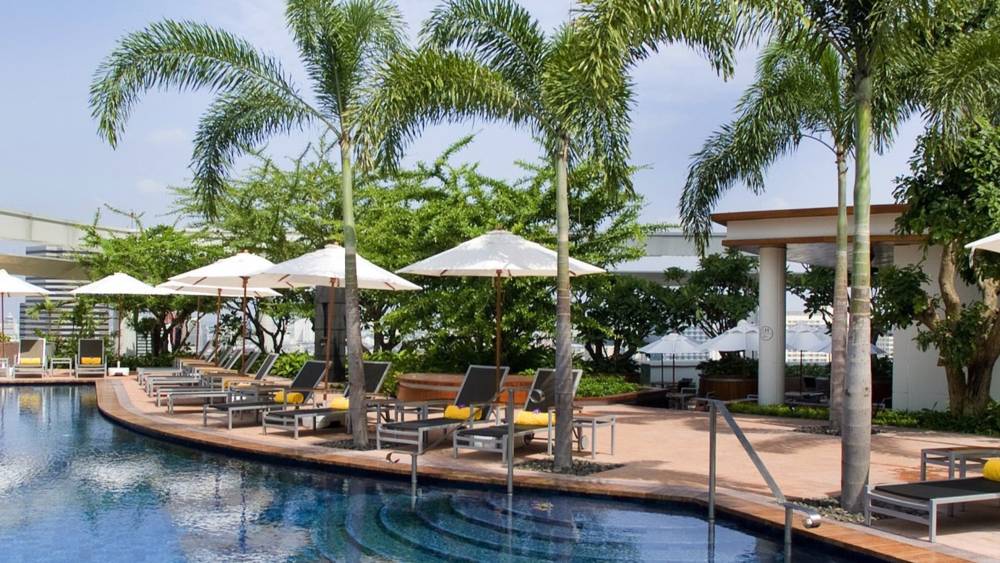The rooftop pool deck at Centara Grand at CentralWorld in Bangkok on a clear afternoon, with palms, loungers and the pool where the Deep House Thailand series runs