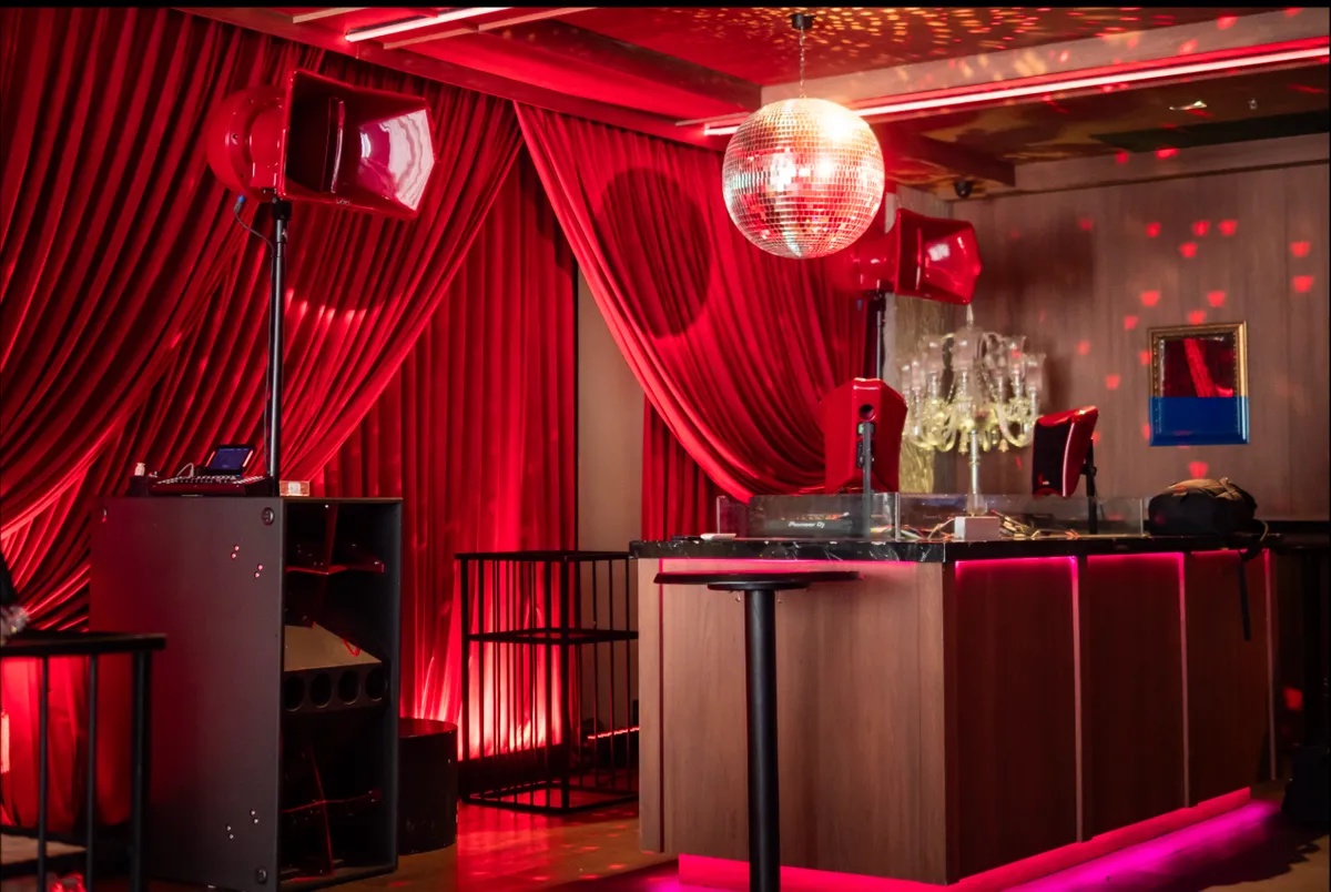 The DJ booth at Baccarat Bangkok, with red velvet curtains, a mirror ball and pink light