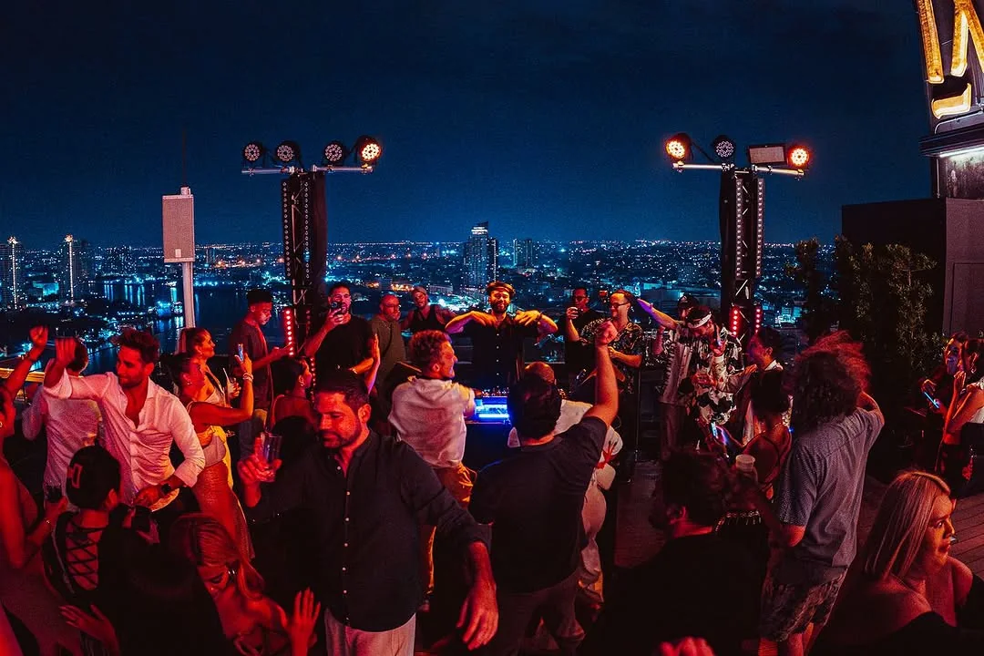The crowd at our previous SIN Rooftop take-over, with Bangkok lit up behind the decks