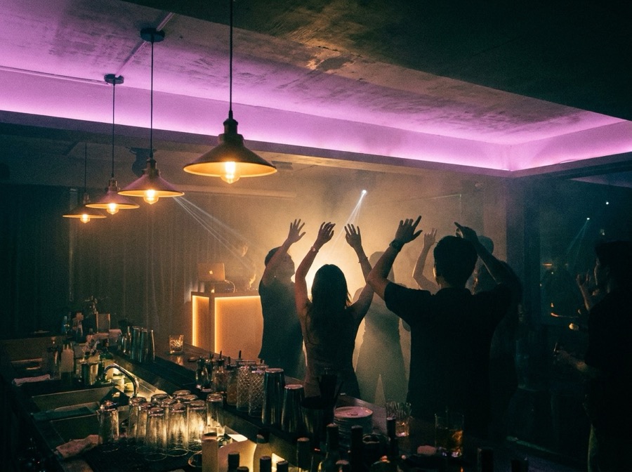 Deep house club night in Bangkok — hands up in a small room with the DJ booth glowing